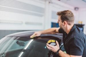 Service man applying wax or coating on car in detailing workshop